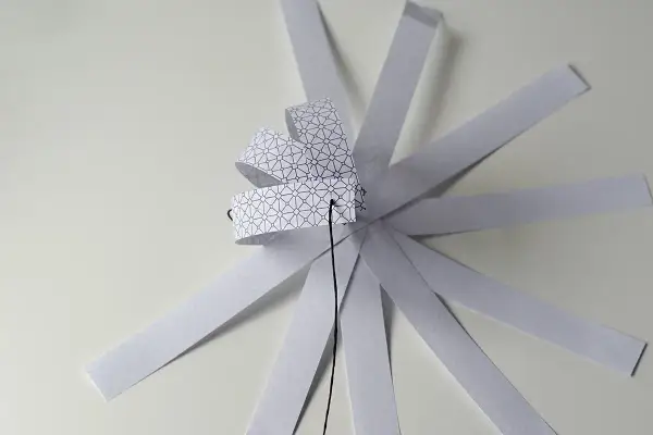 Papierowa ozdoba choinkowa 3D w trakcie tworzenia, z pasków z geometrycznym wzorem.