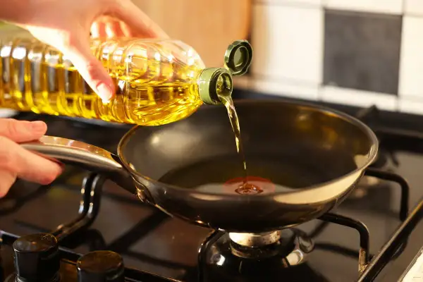 Mano versa olio in padella sul fornello, pronto per friggere.