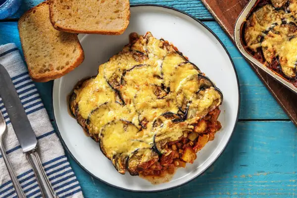 Une part généreuse de moussaka végétarienne, gratinée au fromage, servie avec du pain grillé. Un plat réconfortant et savoureux.