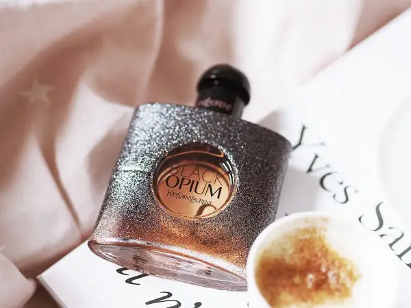Błyszcząca butelka Black Opium od YSL, z nutą **opium floral shock**, obok filiżanki kawy i książki.