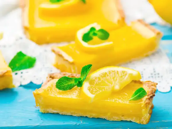Fette di torta fredda al limone, guarnite con fettine di limone e menta fresca, su un tagliere blu.