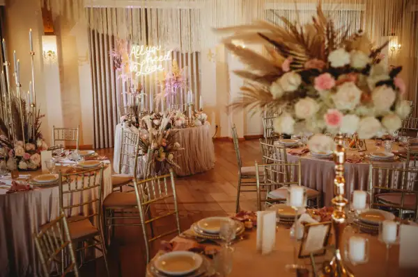 Elegancka sala weselna z neonem "All you need is love". Złote krzesła, pudrowo-różowe obrusy i bujne kwiaty. Zastanawiasz się, ile kosztuje dekoracja sali weselnej?