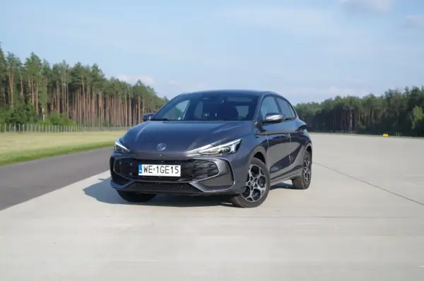 Szary MG3 Hybrid na betonowym placu, z lasem w tle.