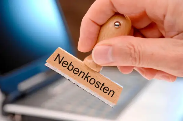 Stempel mit "Nebenkosten" wird über Laptop gehalten. Was darf nicht rein? Klare Regeln für die Nebenkostenabrechnung sind wichtig.