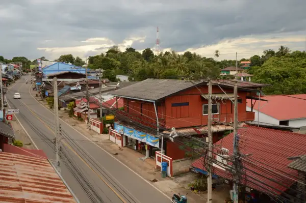 Un pueblo en el Mae Hong Son Loop, con casas rojas y azules a lo largo de una carretera, rodeado de exuberante vegetación y un cielo nublado.