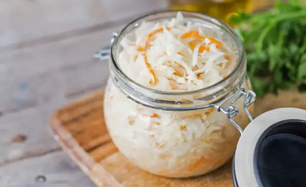 Glas mit Sauerkraut, bereit zum Kohl fermentieren. Frische Kräuter im Hintergrund.