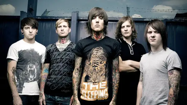 Bring Me The Horizon członkowie, z tatuażami i kolczykami, pozują przed ciemnym tłem.