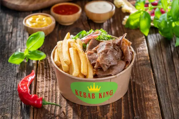 Kebab z frytkami i warzywami w pudełku Kebab King, obok sosów i papryczki chili.