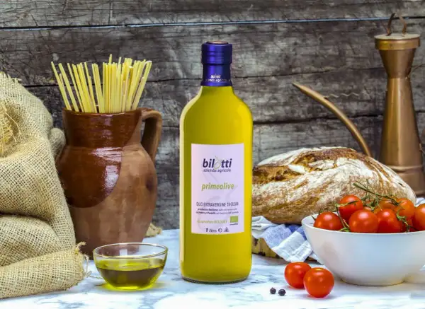 Bottiglia di olio extravergine d'oliva Bilotti, con pasta, pane, pomodorini e una ciotolina di olio, per gustare i migliori tipi di olio.