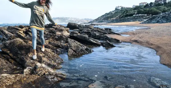 Une jeune femme profite d'une randonnée bord de mer, naviguant sur des rochers près de l'eau.