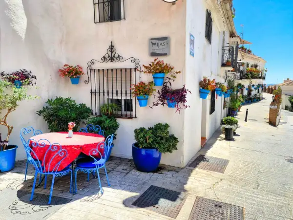 Mesa y sillas azules junto a pared blanca adornada con macetas. Un rincón encantador para descubrir qué ver en Mijas.