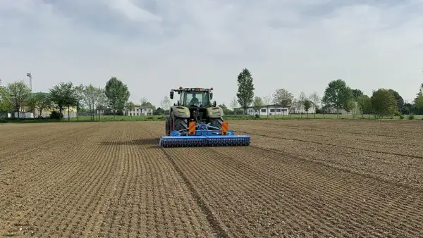 Trattore verde in azione per l'erpicatura del terreno, preparando il campo per la semina.