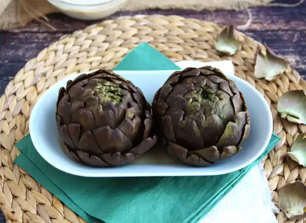 Deux artichauts violets sur une assiette blanche, prêts pour une recette d'artichaut savoureuse.
