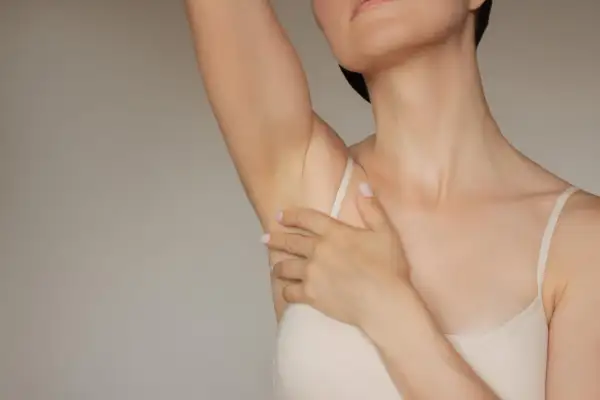 Delikatna skóra pod pachami, gładka dzięki kwasowi glikolowemu. Kobieta dotyka ramienia.