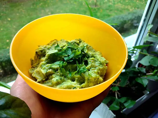 Pyszne guacamole co to? Zielona pasta z awokado, doprawiona świeżą kolendrą, w żółtej miseczce.