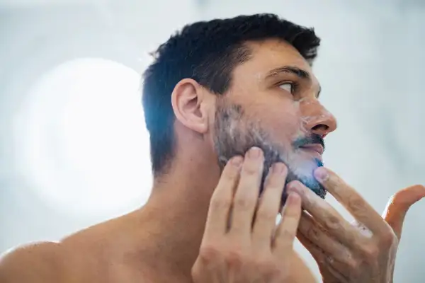 La cara de hombre con espuma de afeitar, preparándose para un afeitado apurado.