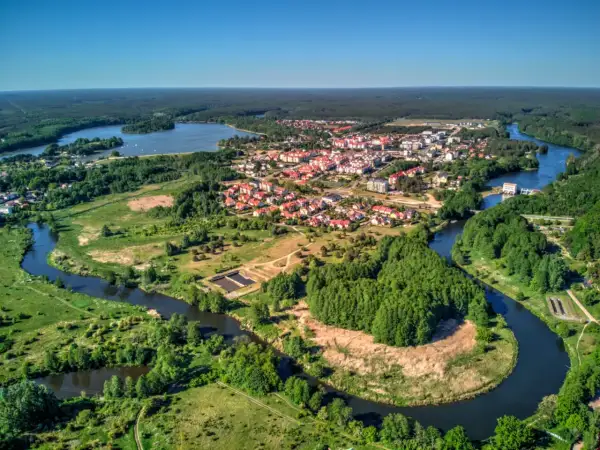 Malownicze miasteczko z czerwonymi dachami rozciąga się nad krętą rzeką, otoczone zielonymi lasami i polami.