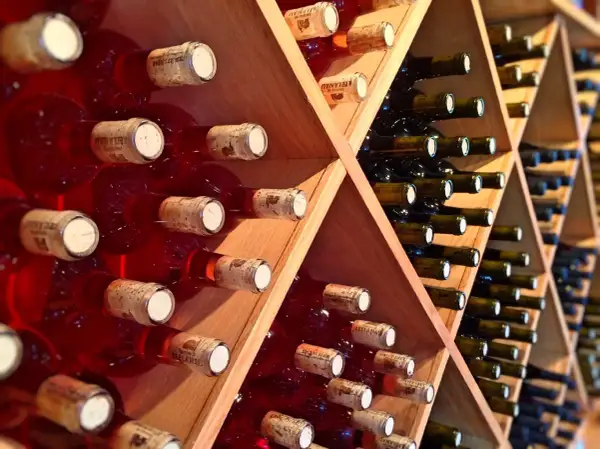 Scaffale in legno con bottiglie di vino rosse e scure, disposte con la corretta inclinazione per la conservazione.
