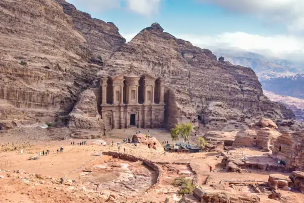 Niezwykłe miasto w skale Jordania, Petra, z monumentalną fasadą wykutą w piaskowcu. Turyści spacerują po piaszczystym placu u stóp starożytnej budowli.