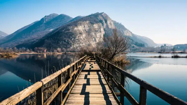 Passerella in legno su lago calmo, montagne sullo sfondo. Un luogo incantevole per scoprire cosa vedere in Franciacorta.