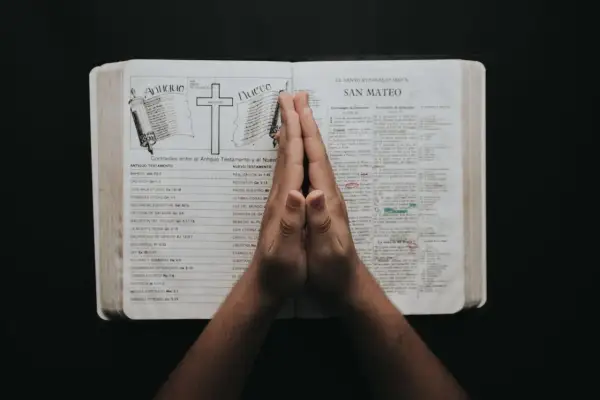Dłonie złożone w geście modlitwy o prośbę nad otwartą Biblią.