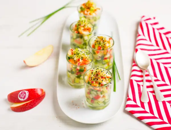 Amuse-bouche pomme et crevettes dans des verrines, garnies de pousses. Des quartiers de pomme Pink Lady sont disposés à côté.