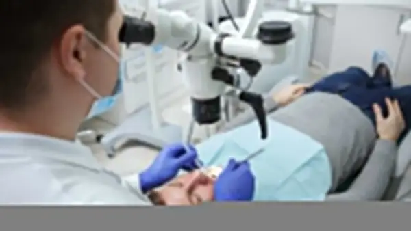 Dentysta pod mikroskopem bada ząb pacjenta. Po leczeniu kanałowym można jeść, ale warto poczekać na znieczulenie.
