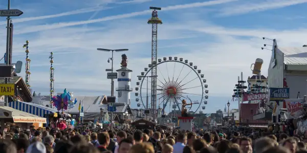 Menschenmassen auf dem **Bayern Oktoberfest** mit Riesenrad, Fahrgeschäften und Bierkrügen.