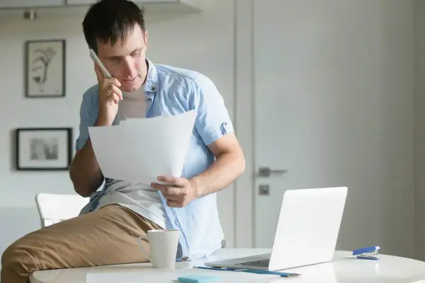 Uomo al telefono con fogli in mano, preoccupato per una busta paga errata in eccesso.