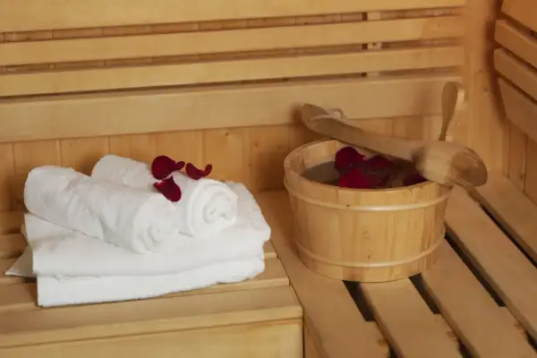 Białe ręczniki i drewniane wiaderko z wodą i płatkami róż w saunie. Dylemat: najpierw sauna sucha czy parowa?