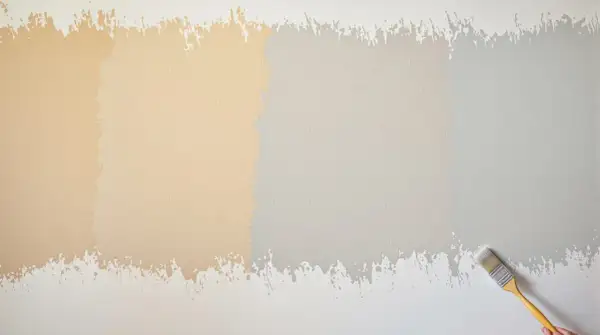 Échantillons de peinture sur un mur texturé, montrant 2 ou 3 couches de peinture dans des tons de beige et de gris. Un pinceau est visible à droite.