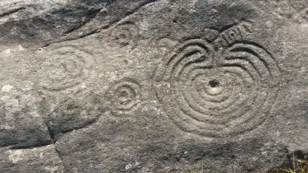 Petroglifos de Mogor: grabados circulares concéntricos y un posible sol en una roca antigua.