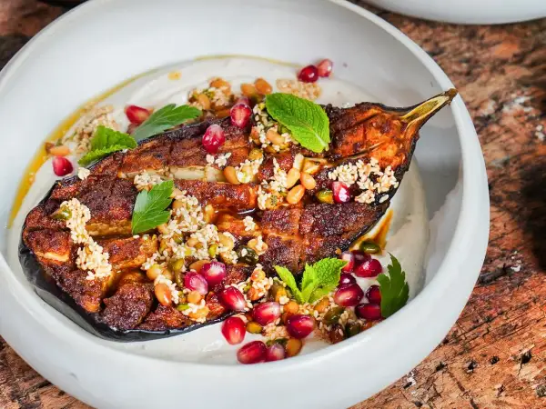 Gebackene Aubergine mit Tahini, Granatapfelkernen und Minze. Ein köstliches Gericht, das zeigt, wie vielseitig auberginen rezepte im backofen sein können.