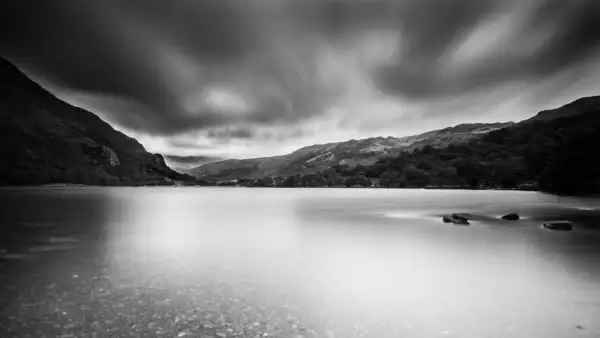 Un photographe paysage capture un lac paisible sous un ciel dramatique, les montagnes se reflétant dans l'eau lisse.