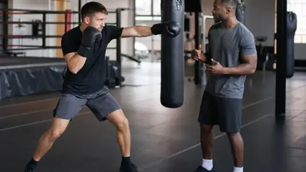A boxer practices jabs with a trainer watching, counting the punches. The gym has boxing numbers on the wall.