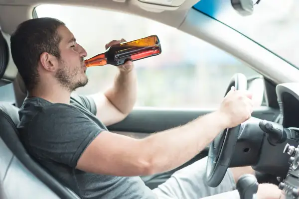 Mężczyzna pije piwo za kierownicą. To niebezpieczna jazda po alkoholu, która może skończyć się tragicznie.