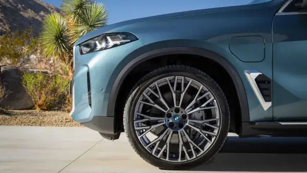 Nowe BMW X5 2023 w kolorze niebiesko-zielonym, z felgami o skomplikowanym wzorze, zaparkowane na tle pustynnego krajobrazu.