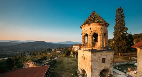 Wieża dzwonnicza Gelati Monastery na tle górskiego krajobrazu o zachodzie słońca.