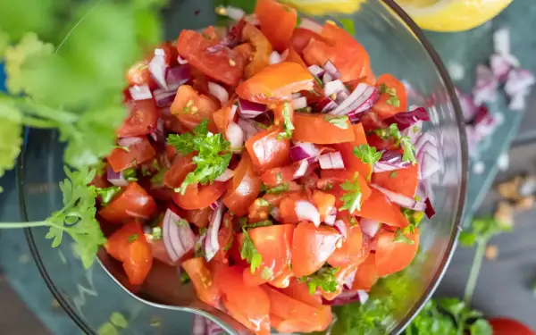 Frischer tomatensalat mit zwiebeln und Petersilie in einer Glasschüssel, garniert mit Koriander.