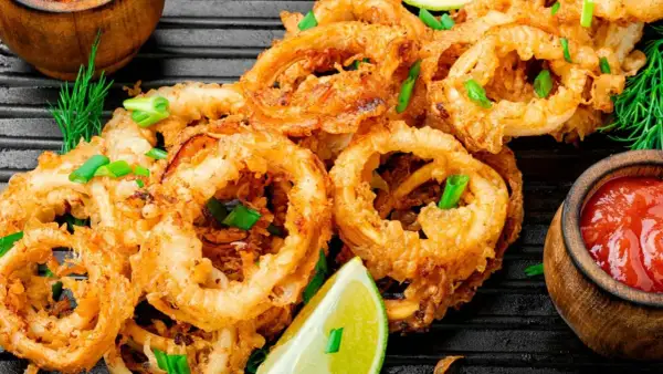 Crujientes calamares en salsa, adornados con cebolleta y lima, listos para disfrutar.