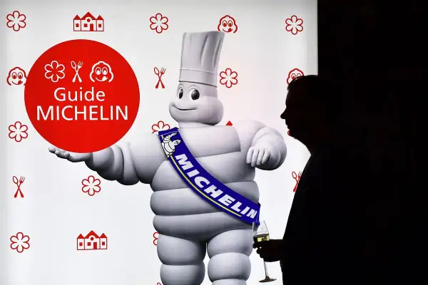 El muñeco Michelin, con su banda "MICHELIN", posa junto a un hombre con copa. Un símbolo de los restaurantes con estrella Michelin.