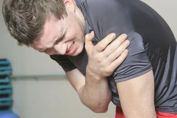 Mężczyzna z bólem trzyma się za ramię, cierpiąc z powodu naderwanego bicepsa po treningu.
