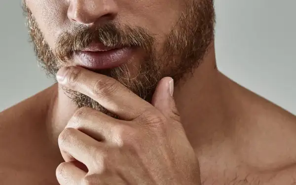Gros plan sur un homme pensif, sa main caressant sa barbe. L'évolution de sa barbe, de la naissance à sa forme actuelle, est visible.
