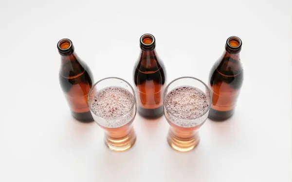Tre bicchieri di birra con schiuma e quattro bottiglie marroni vuote, una birra andata a male.