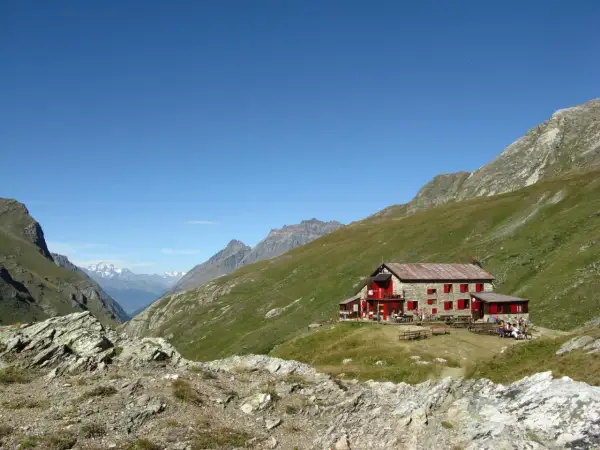 Rifugio nel Val di Rhemes, con persone sedute ai tavoli all'esterno, circondato da verdi pendii montuosi sotto un cielo azzurro.