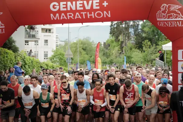 Des coureurs se préparent au départ de la course 10km Genève, sous une arche rouge "Genève + Marathon".