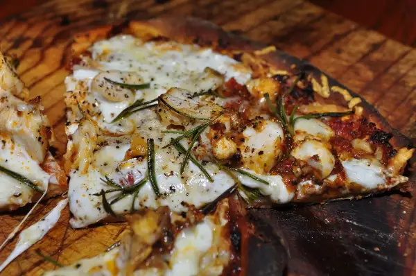 En närbild av en utsökt pizza med kyckling, ost och rosmarin. En smak av pizzans ursprung.
