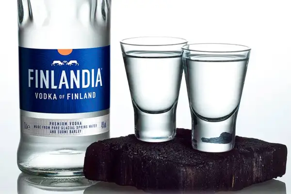 Butelka wódki Finlandia i dwa kieliszki z wódką na ciemnym tle.