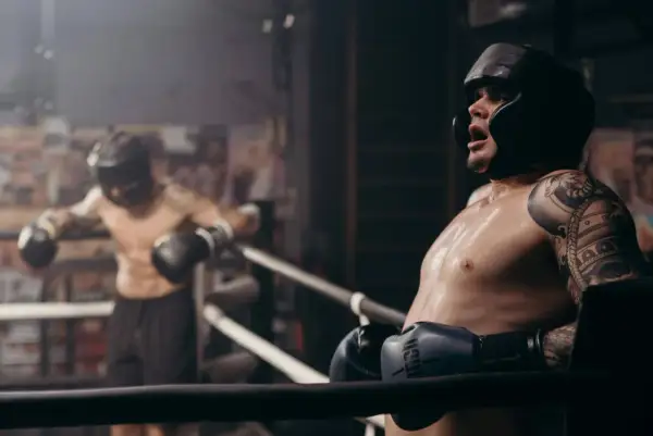 Two boxers in a ring, one leaning on the ropes, sweat glistening. This intense roadwork boxing session shows the grit and determination of the fighters.