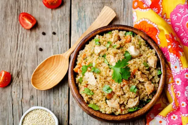 Una ciotola di quinoa con pollo e verdure, un piatto ricco di quinoa valori nutrizionali, su un tavolo di legno con pomodorini e un cucchiaio.